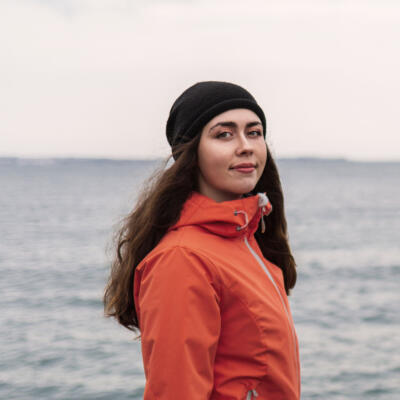 Frau mit Windjacke und Mütze steht am See